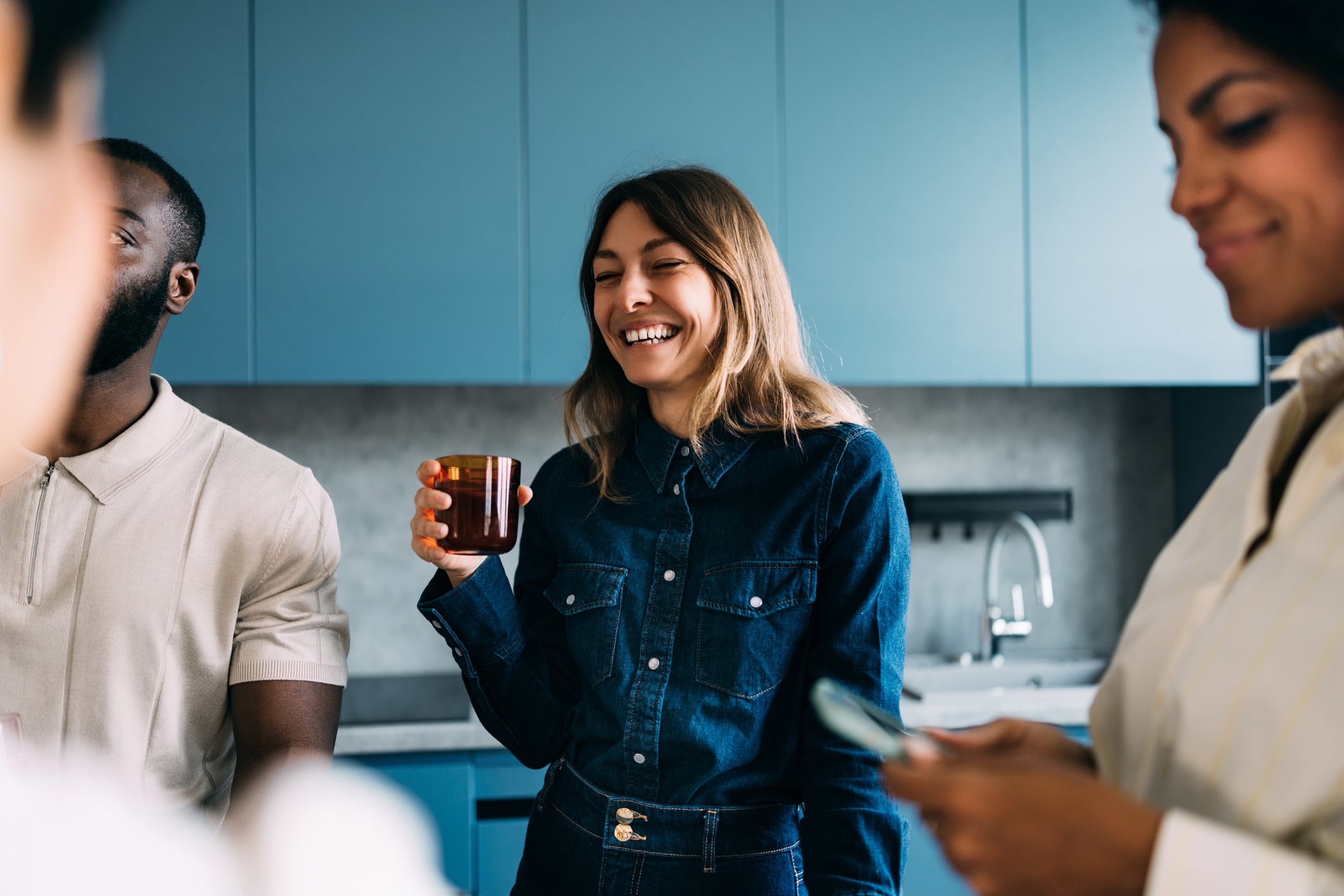 Four people are enjoying a casual gathering in a modern kitchen, showcasing bond, warmth, and friendship. The image presents laughter, interaction, and togetherness, emphasizing a harmonious and relaxed environment.