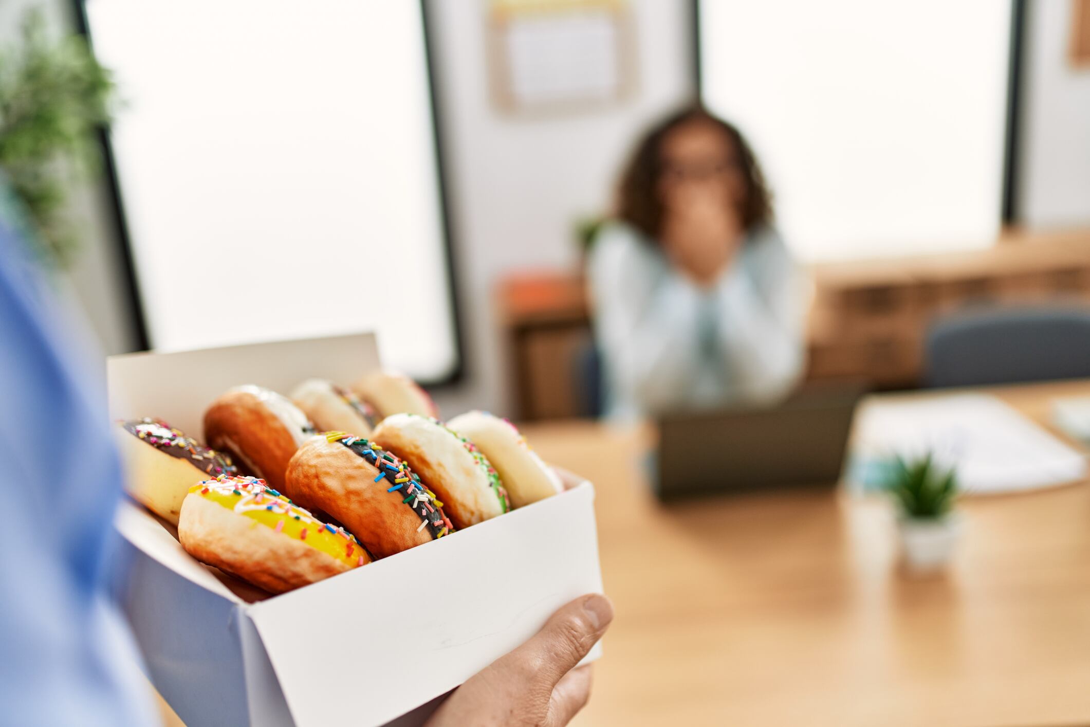 Two middle age business workers working at the office. Man holding box with doughnuts to his partner.