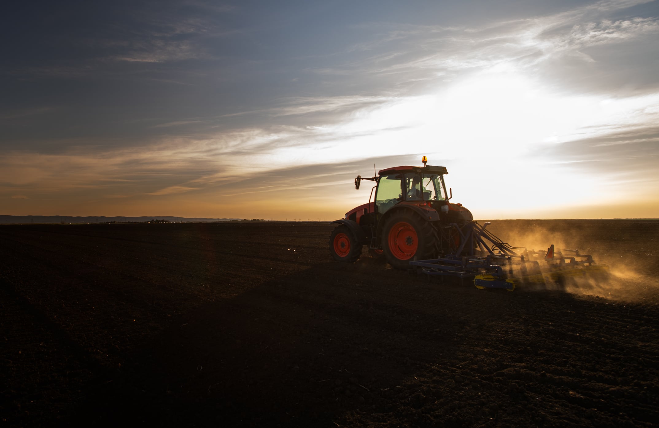 Tractor plowing farm, preparing soil for new crop plantation during the evening.