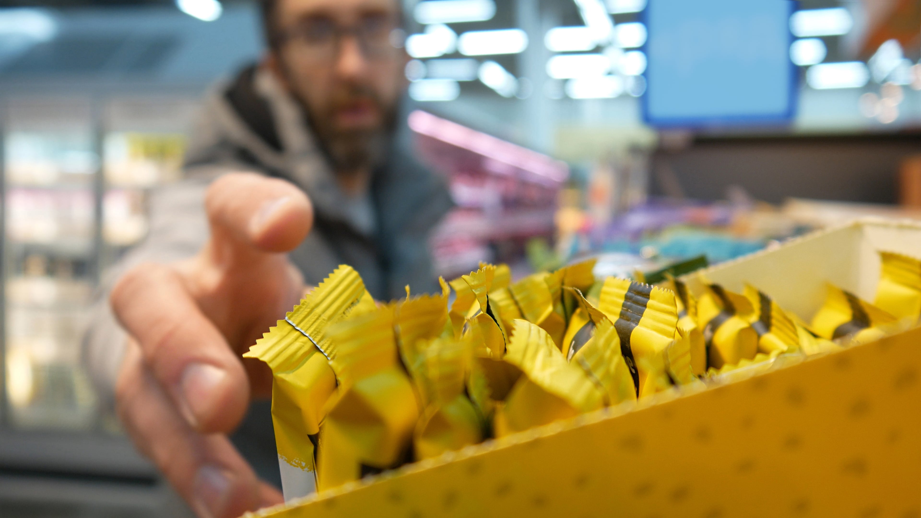A man reaching the hand to take a protein bar from a supermarket shelf close-up.