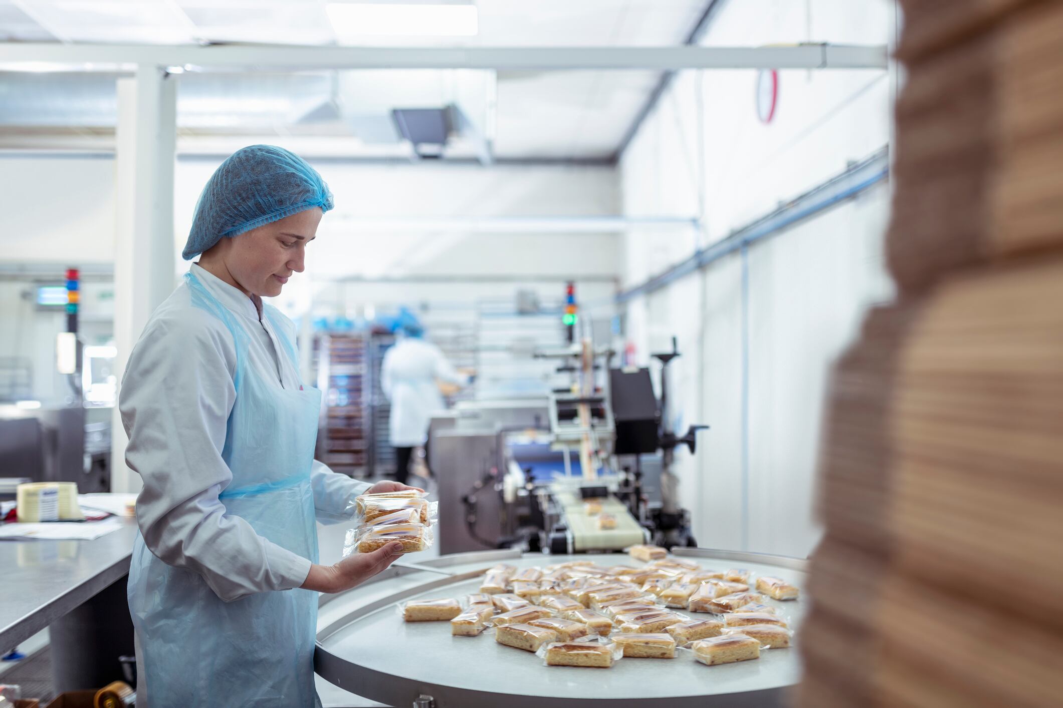 Worker with tray bake cakes on packing line in cake factory