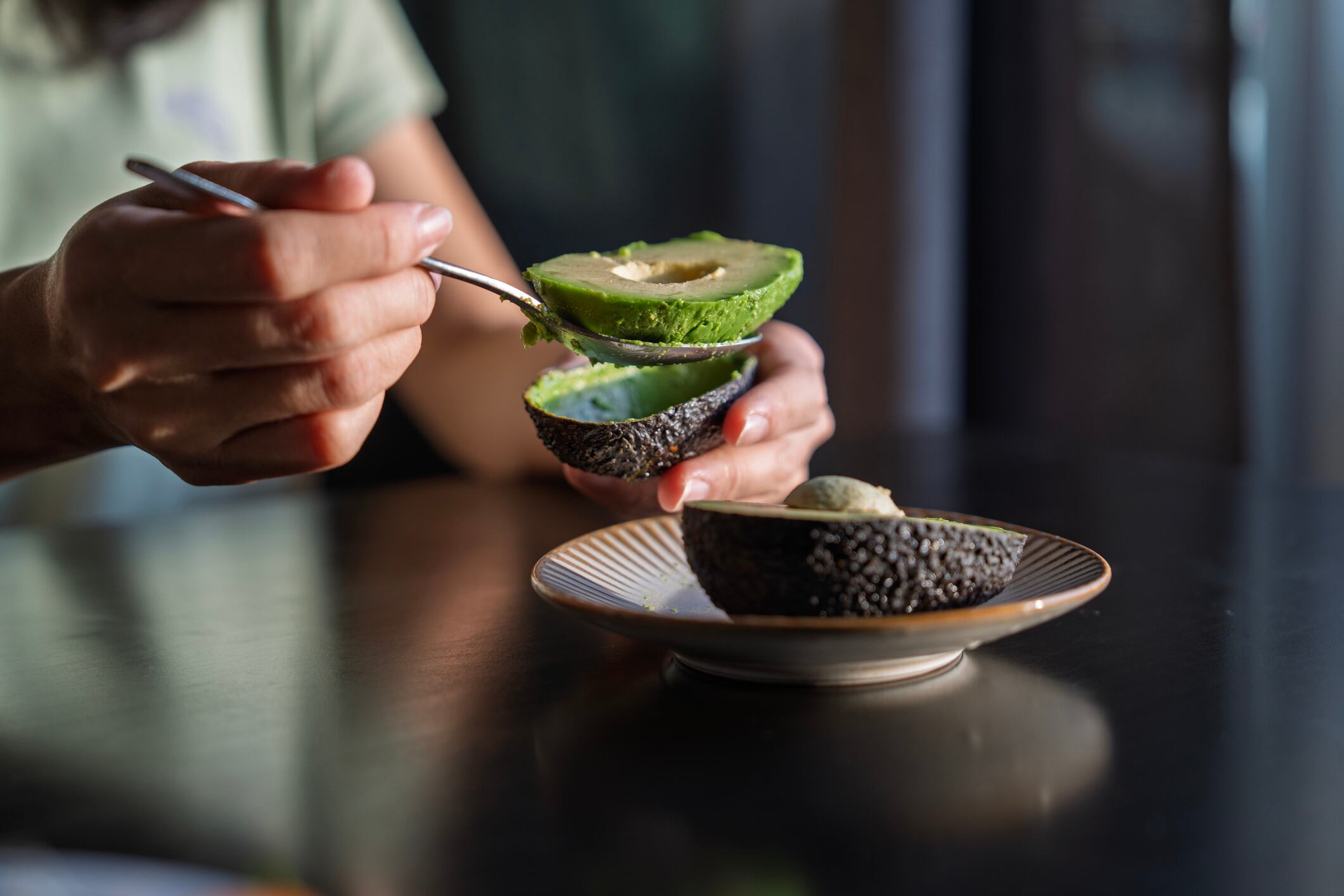 A close-up captures hands using a spoon to scoop the vibrant green flesh from a freshly halved avocado, healthy eating.