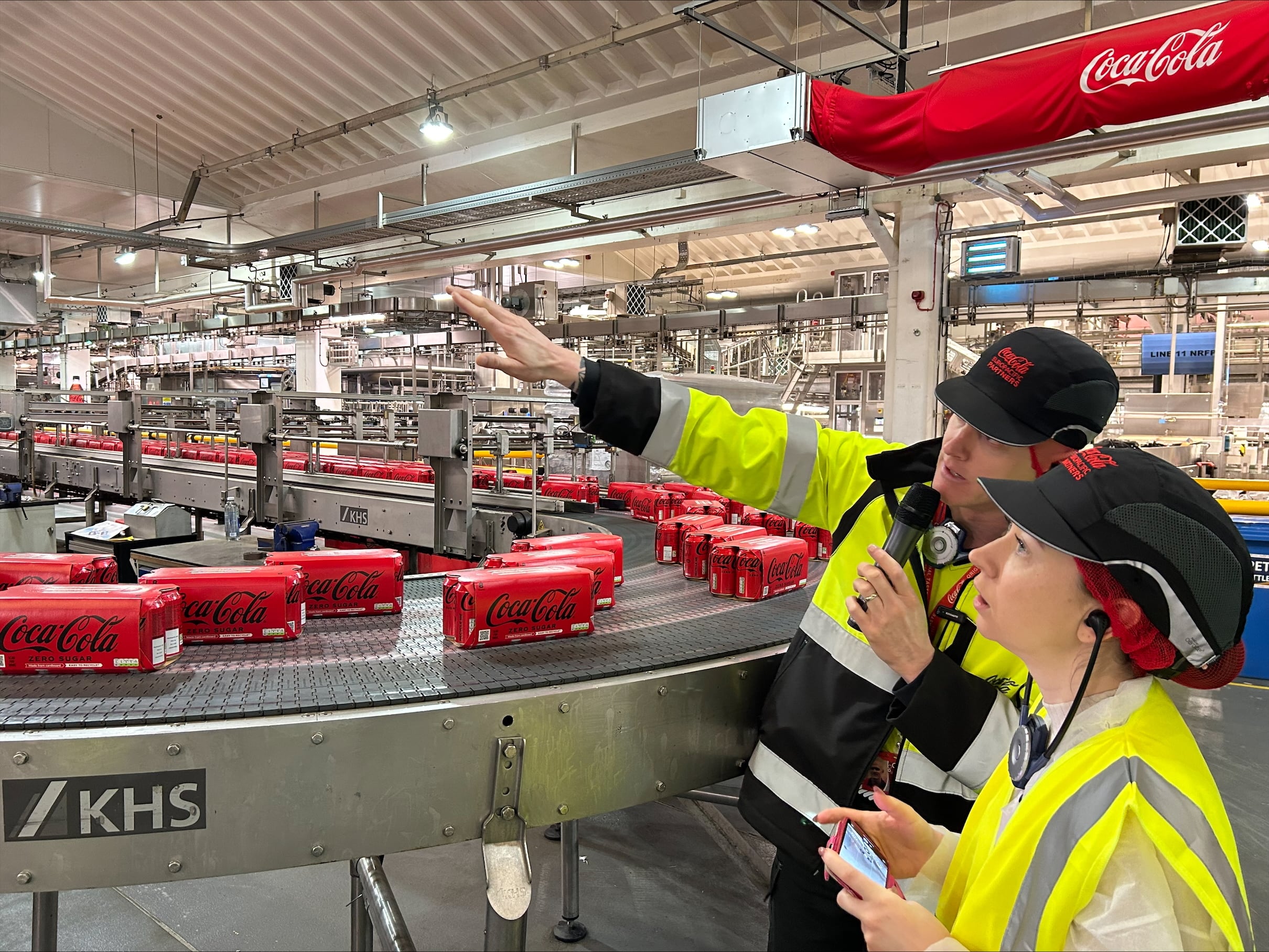 A woman listening to a presenter talk in cola factory.