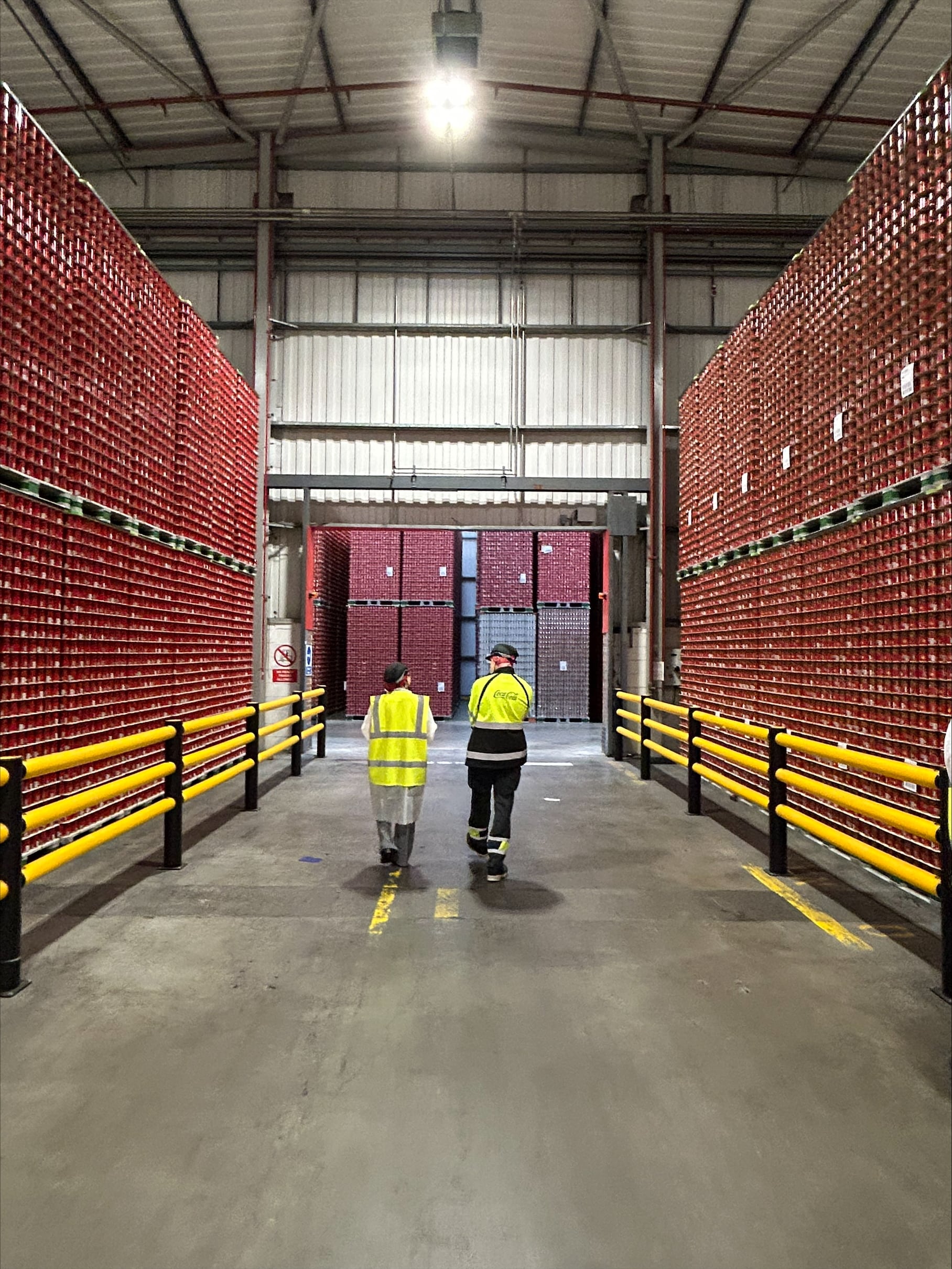 Two people walking between stacked pallets of cans.