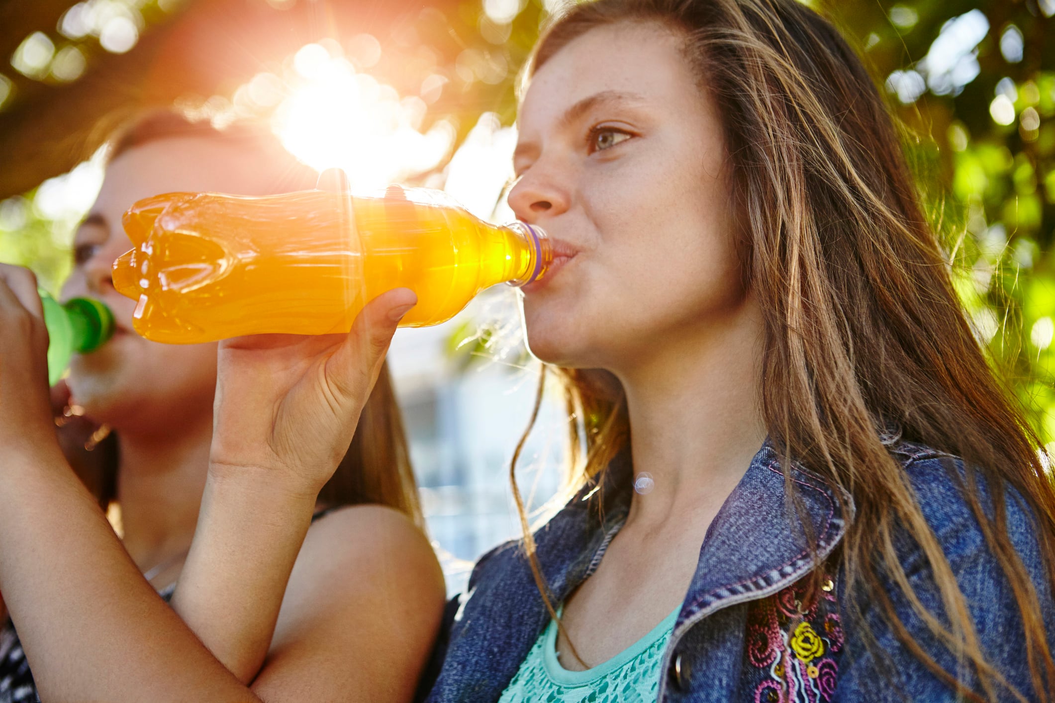 Two female friends sitting outdoors, drinking soft drinks