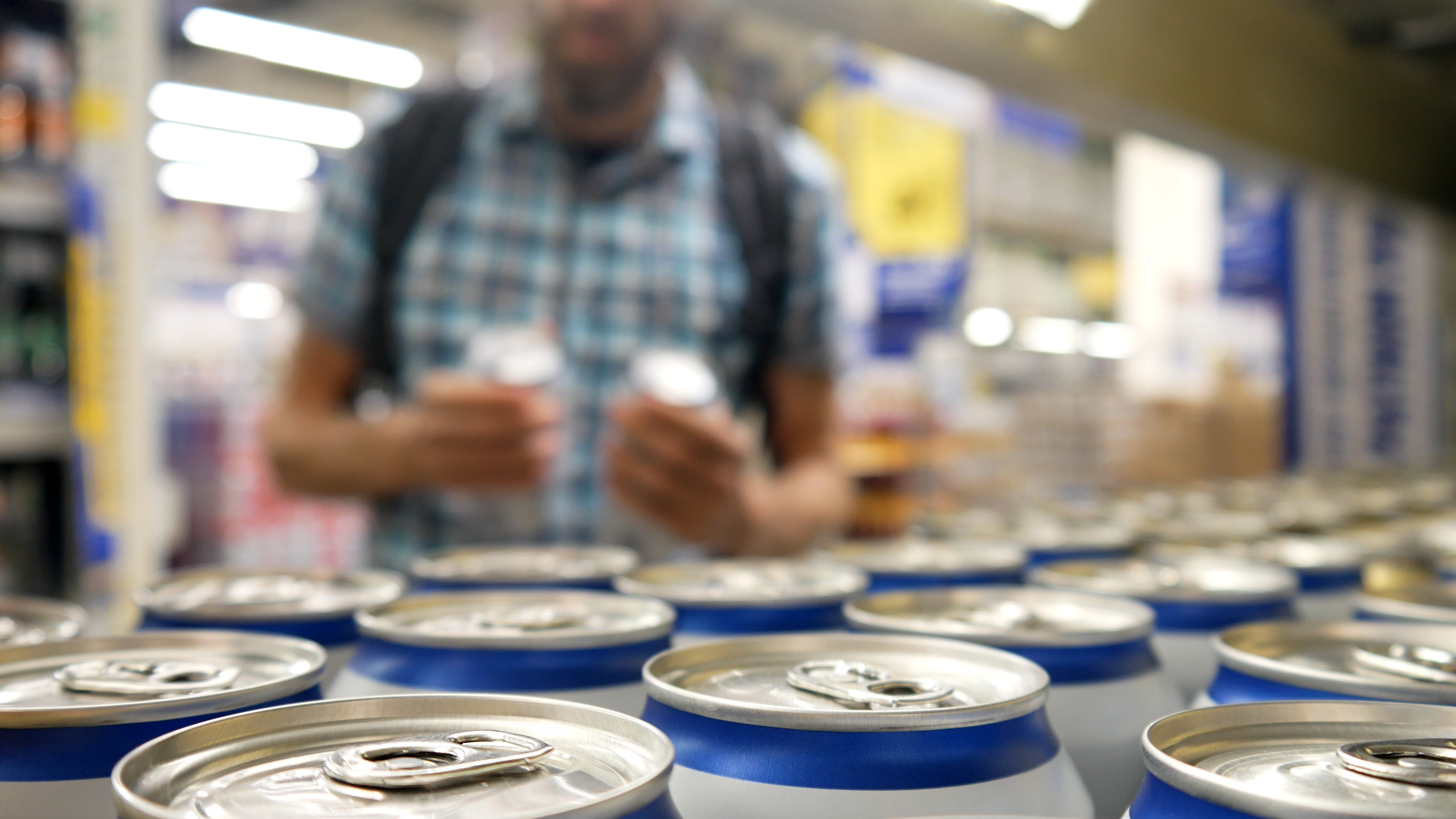Many aluminium cans of beer or another drink on a store shelf and a male buyer takes a couple