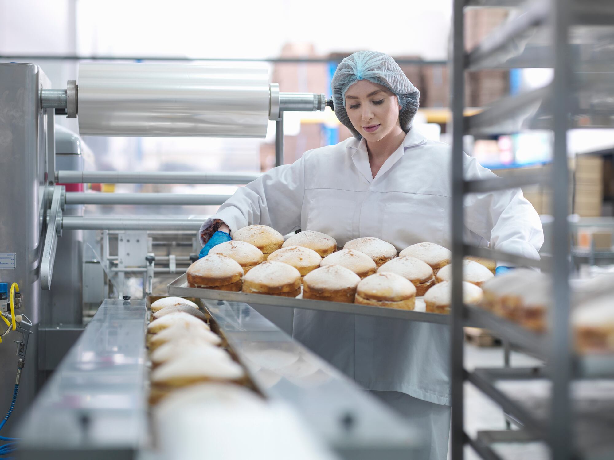 Woman with tray of baked goods in factory.