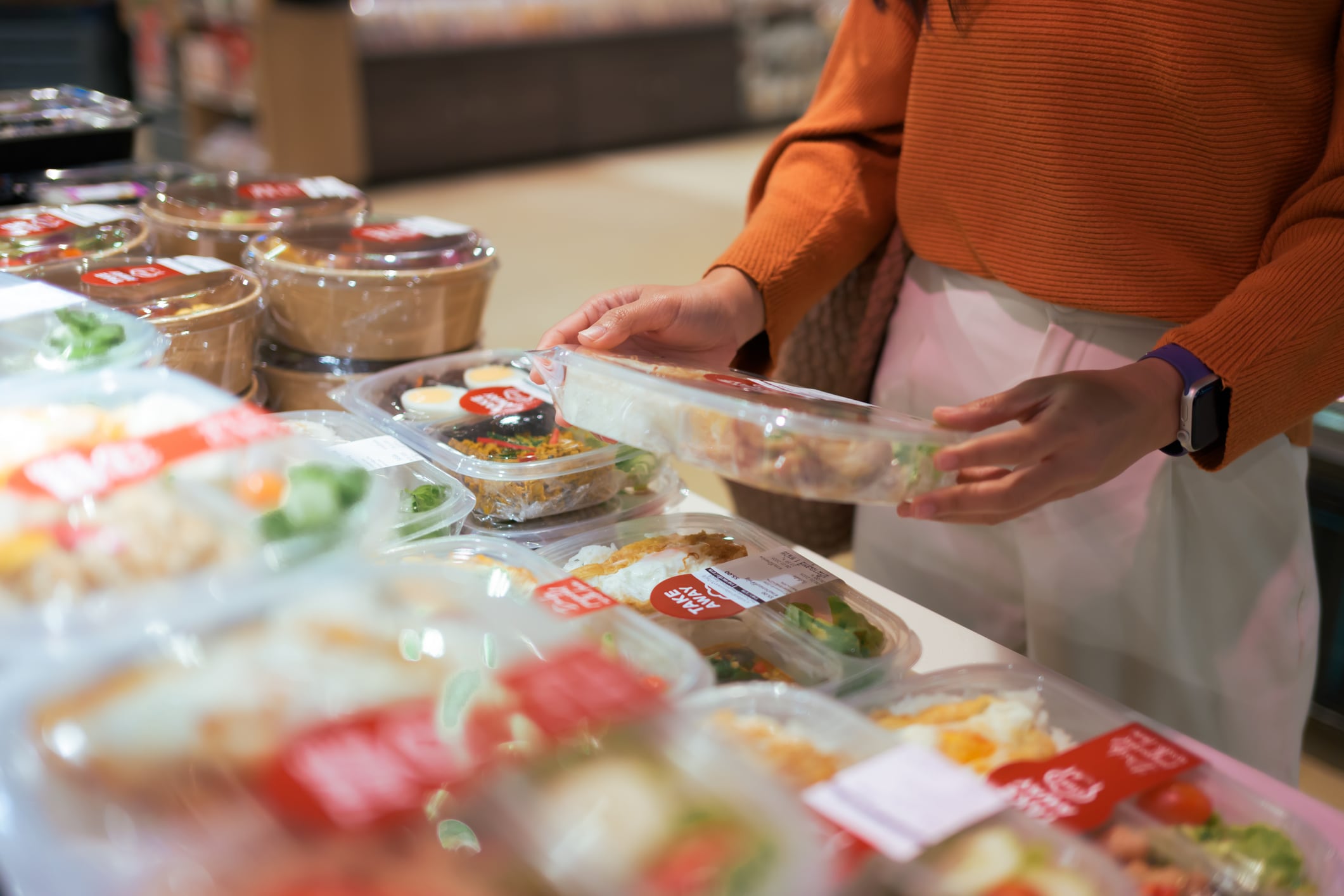 Customer selecting a convenient grab and go bento box from a supermarket deli, offering quick lunch and dinner meal solutions