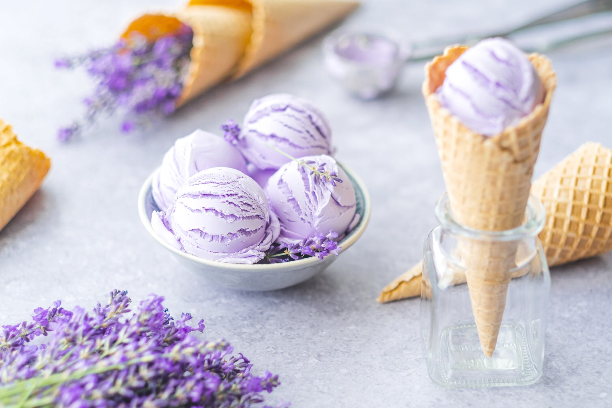 Creamy natural purple ice cream scoops in a bowl with flowers on gray background. Frozen Dessert.