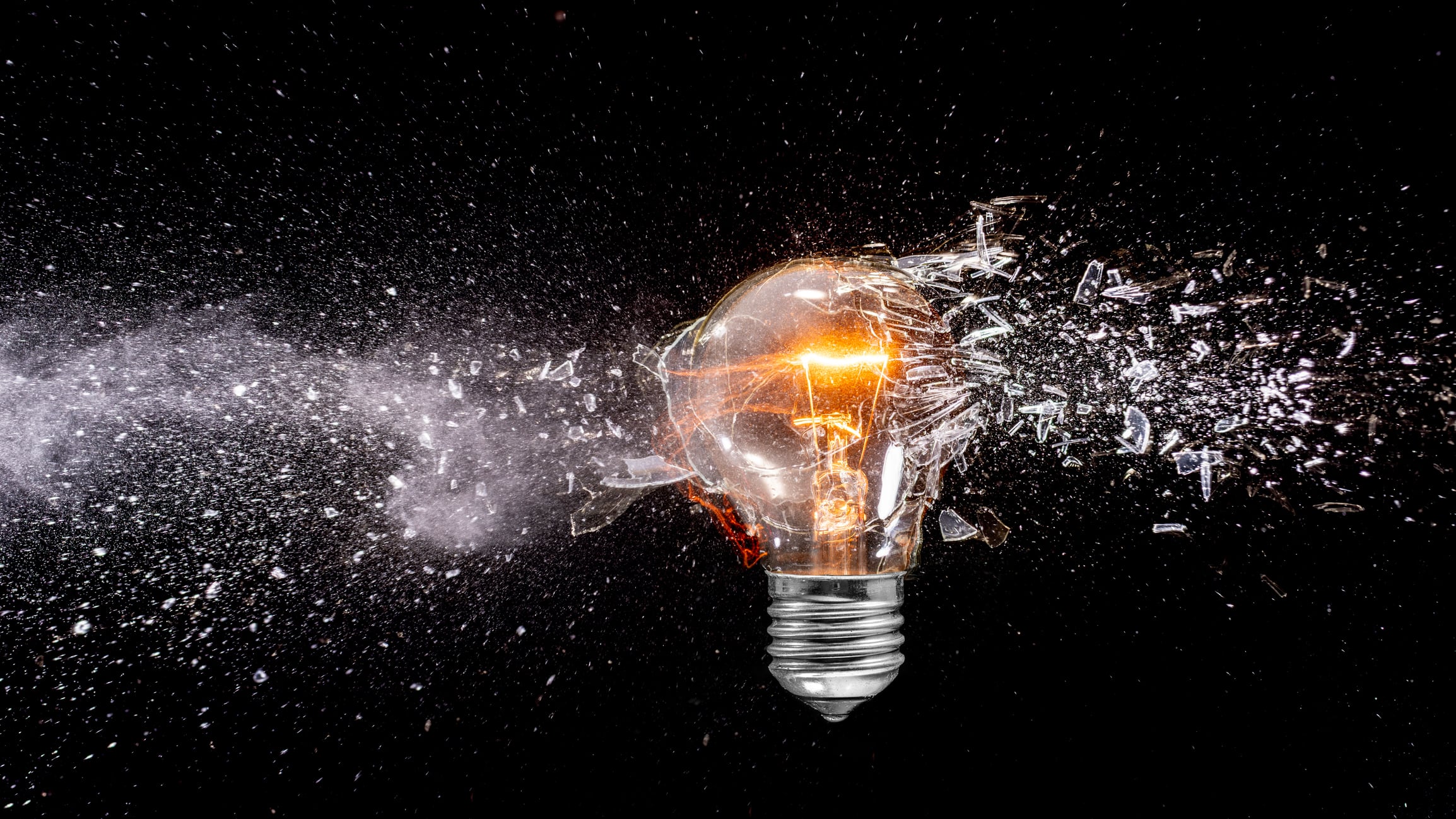 Light bulb exploding creating shattered glass and powder on dark background