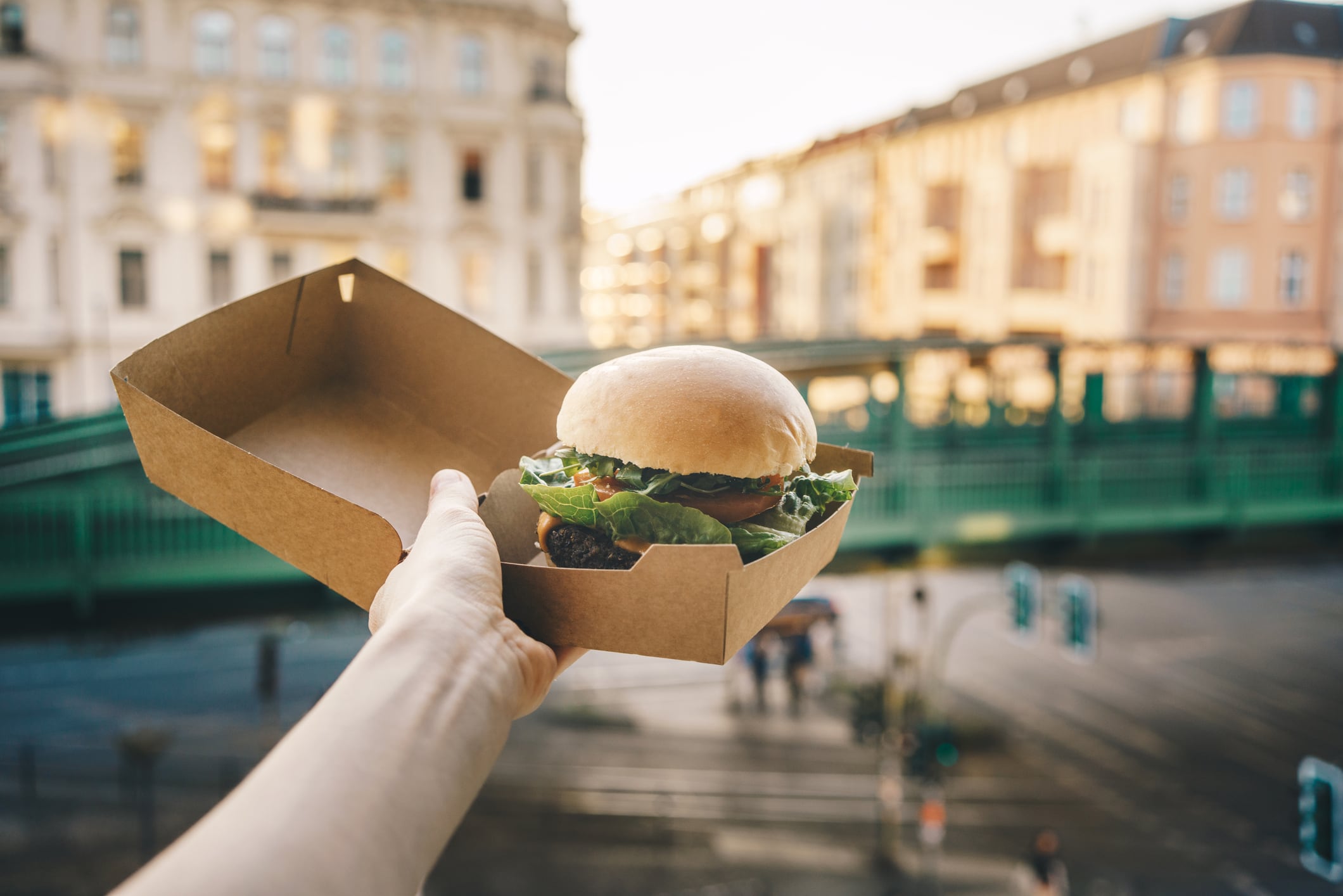 Woman holding a burger in take out box in front of the open window, coronavirus lockdown concept