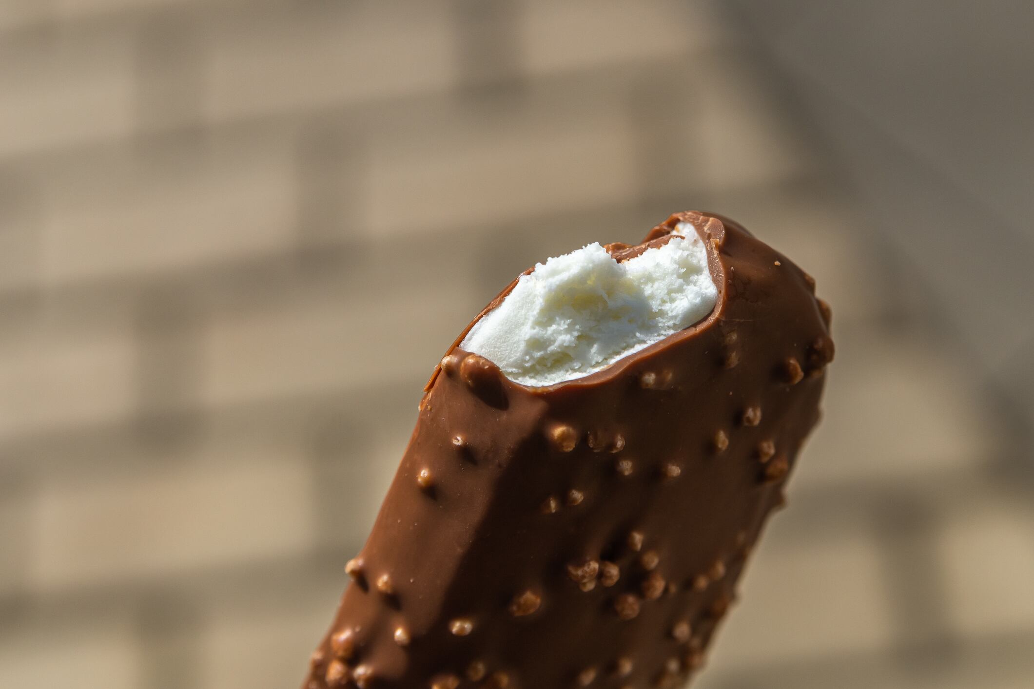 Bitten off white ice cream covered with milk chocolate with nuts. Warm shades. Blurry background. Food. Sweets. A treat.