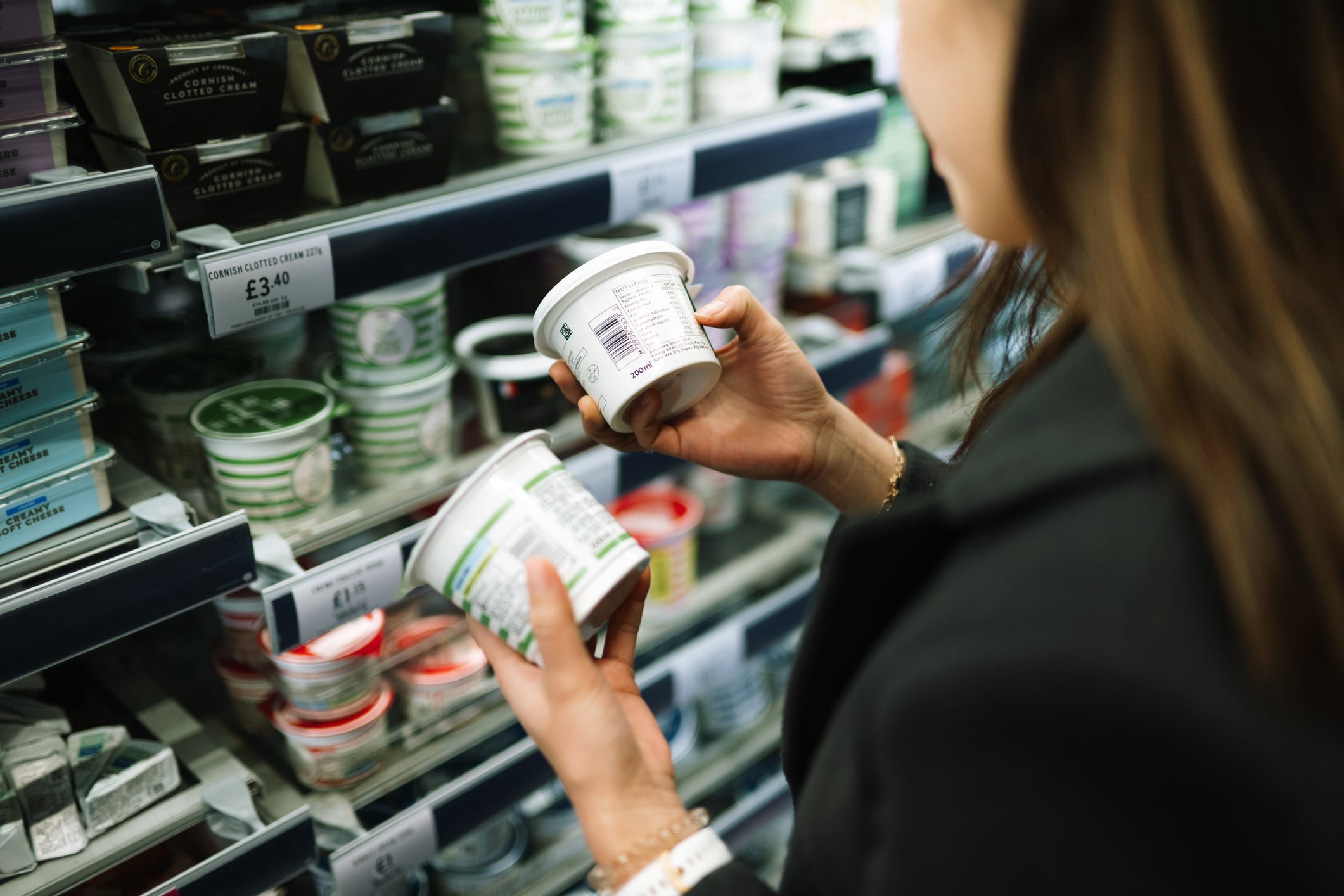 A detailed view of a consumer's hands holding two food containers to compare ingredients and health facts while shopping in a modern grocery store.