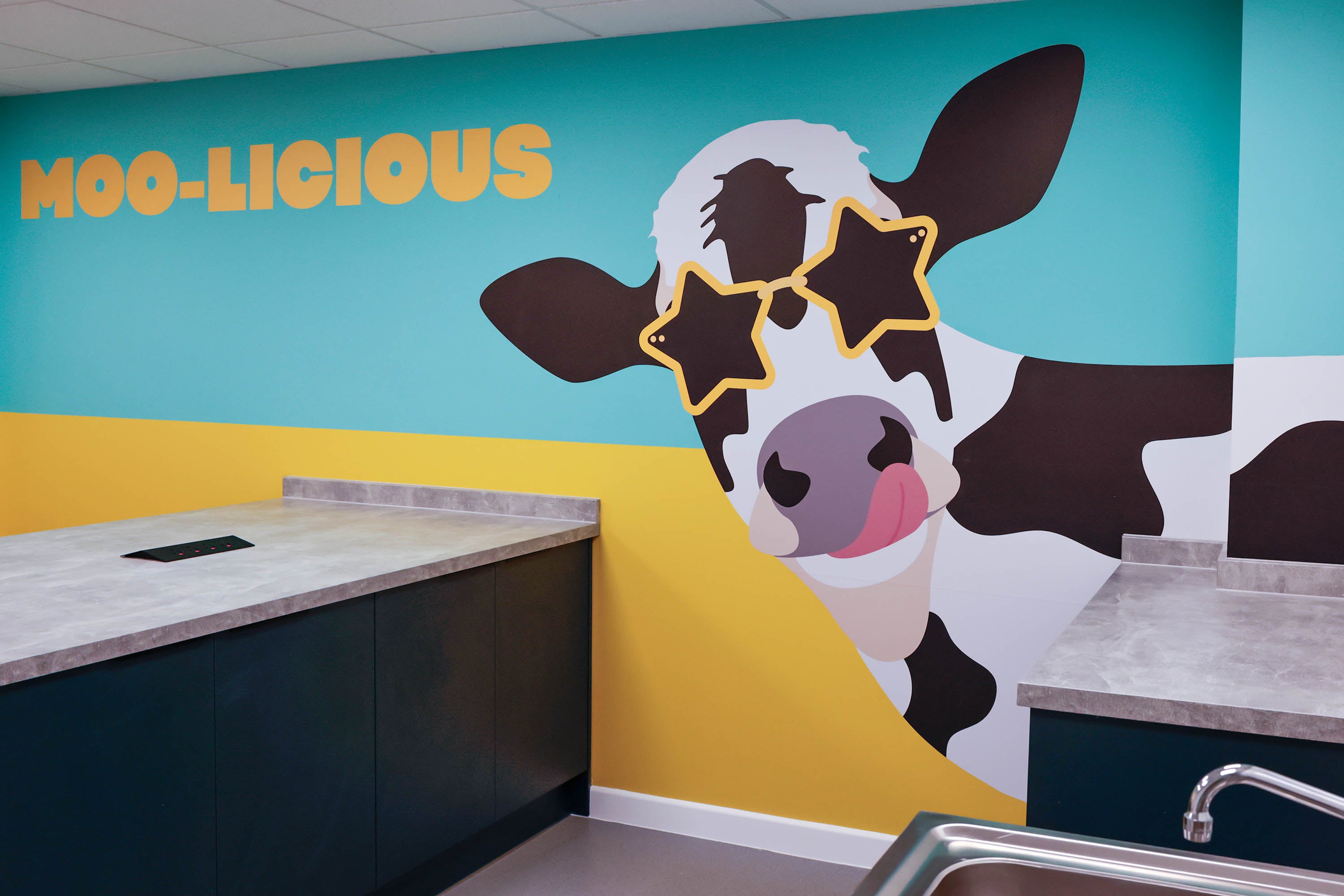 Cow decorated on blue and yellow wall with words 'Moo-licious'