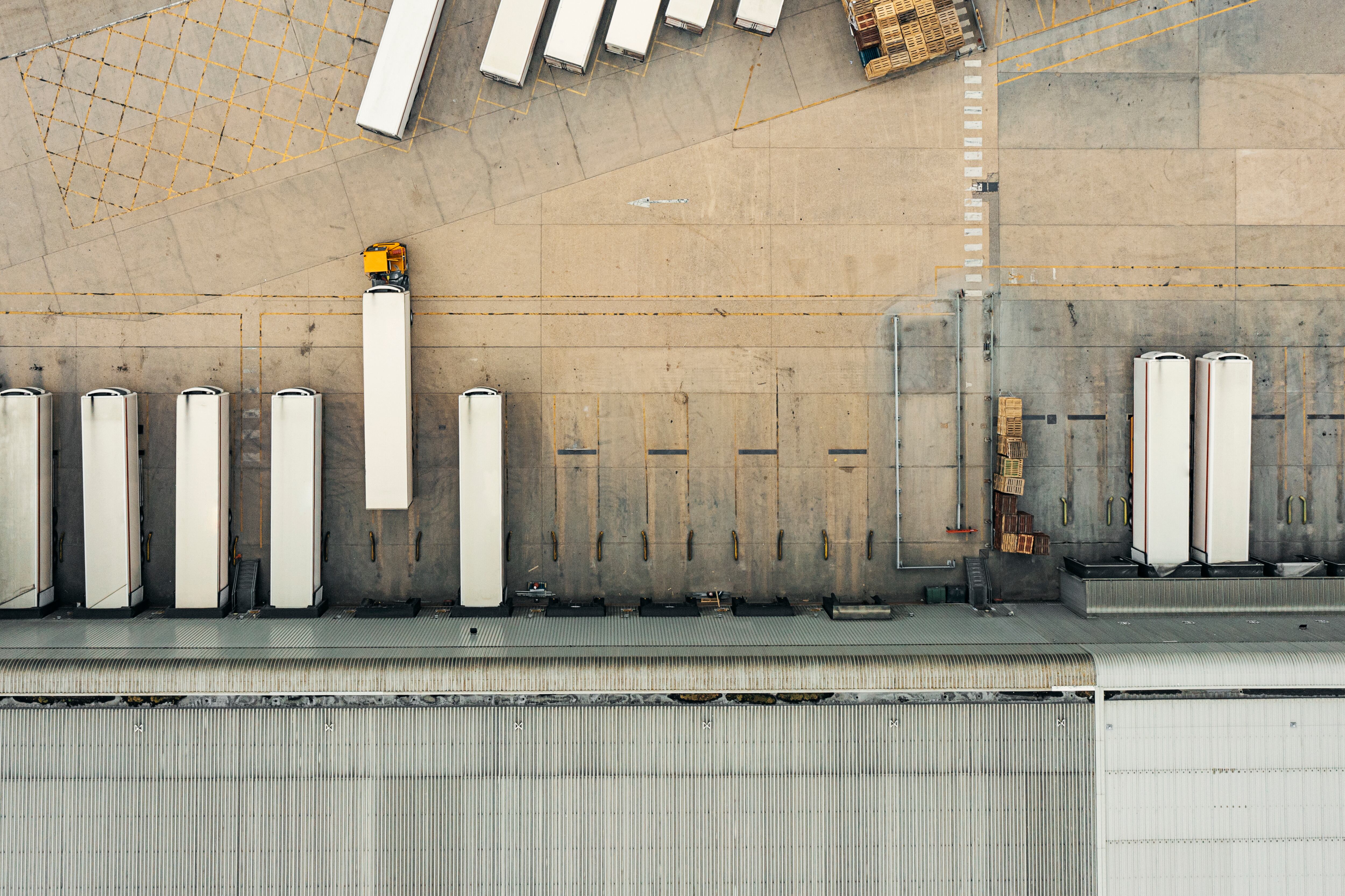 An overhead drone view down onto a distribution warehouse. Articulated lorries are loading/unloading in the loading bays