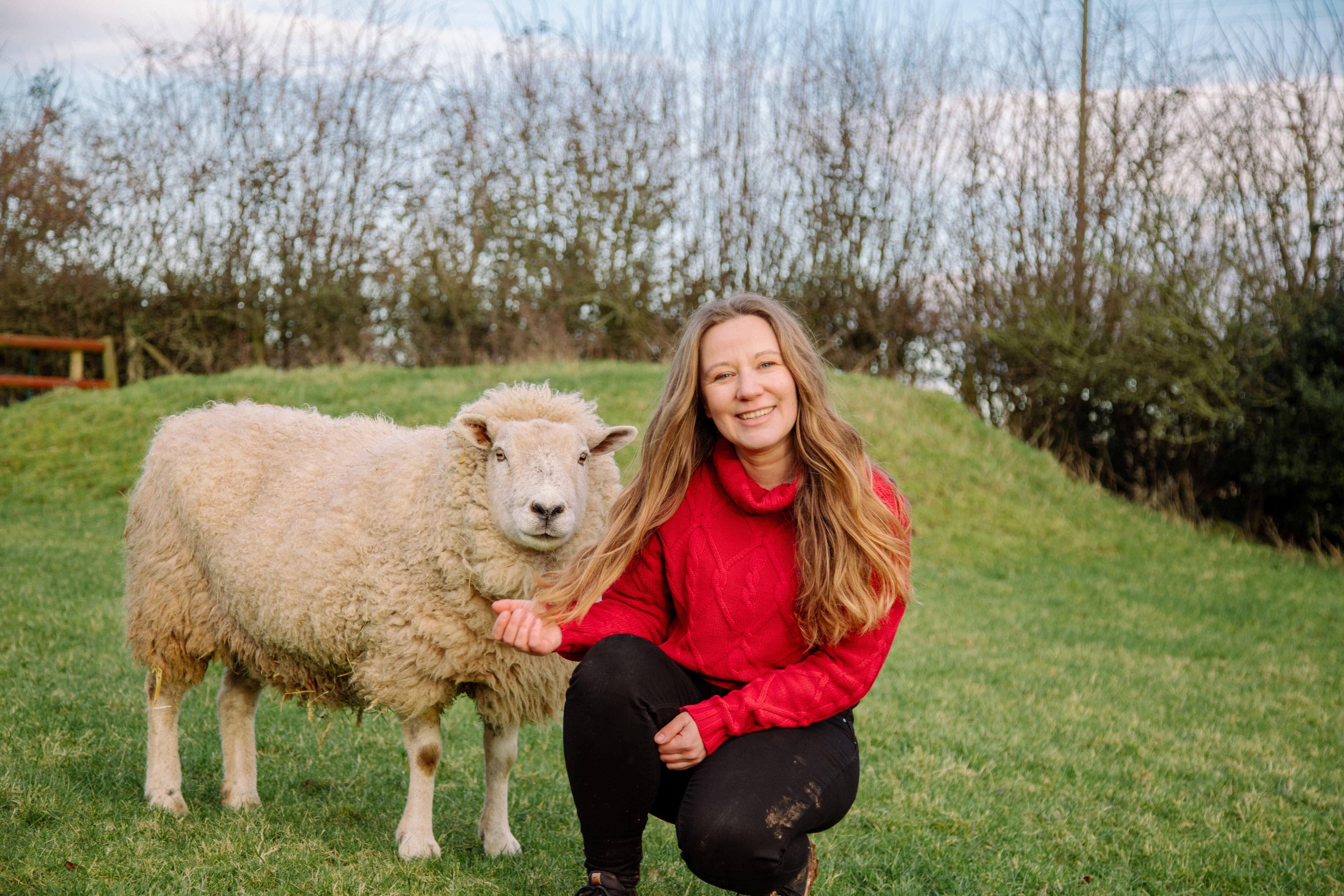 Laura Hellwig, managing director at Viva! kneeling with a sheep.