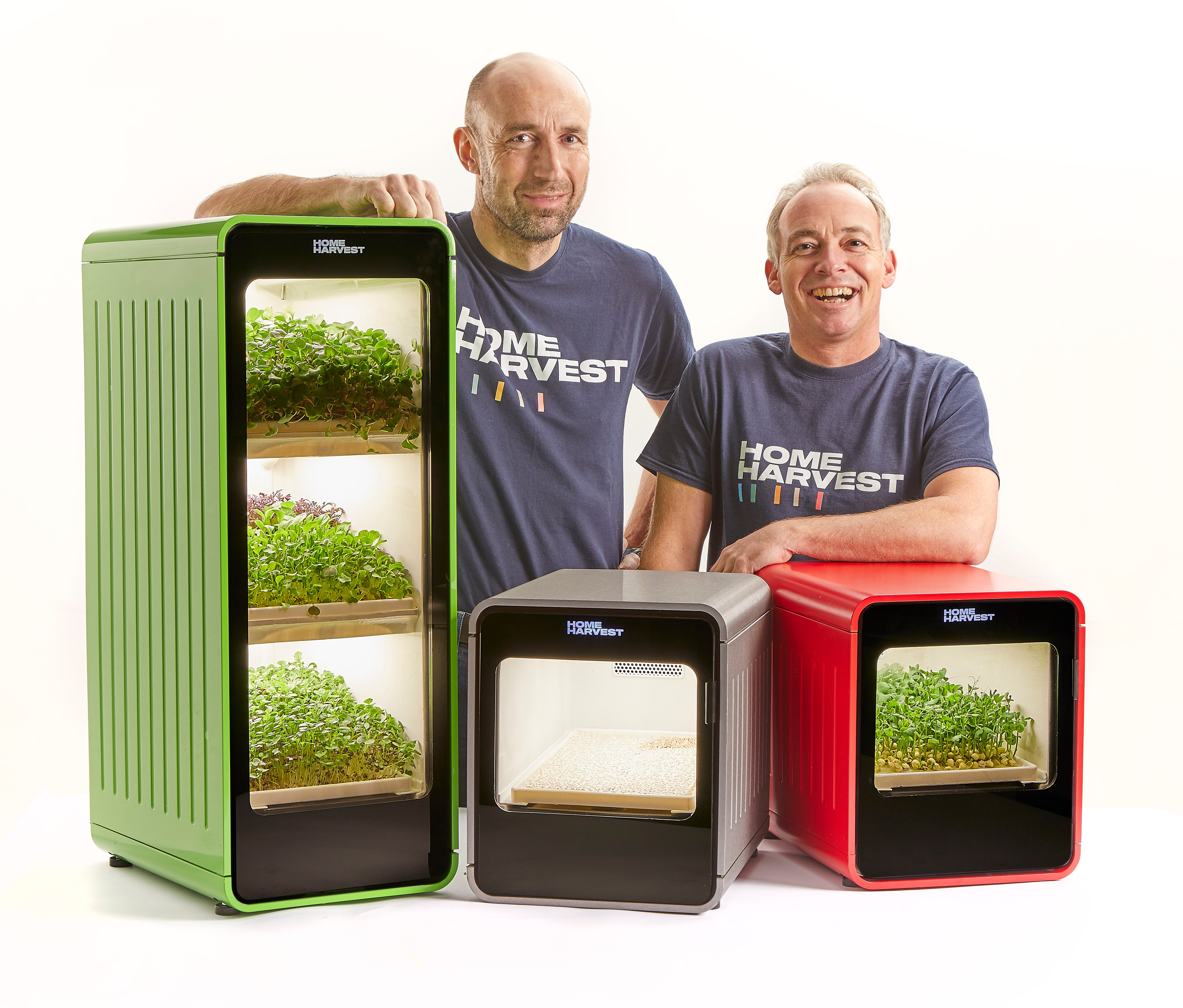 Two men standing with three units growing crops inside.