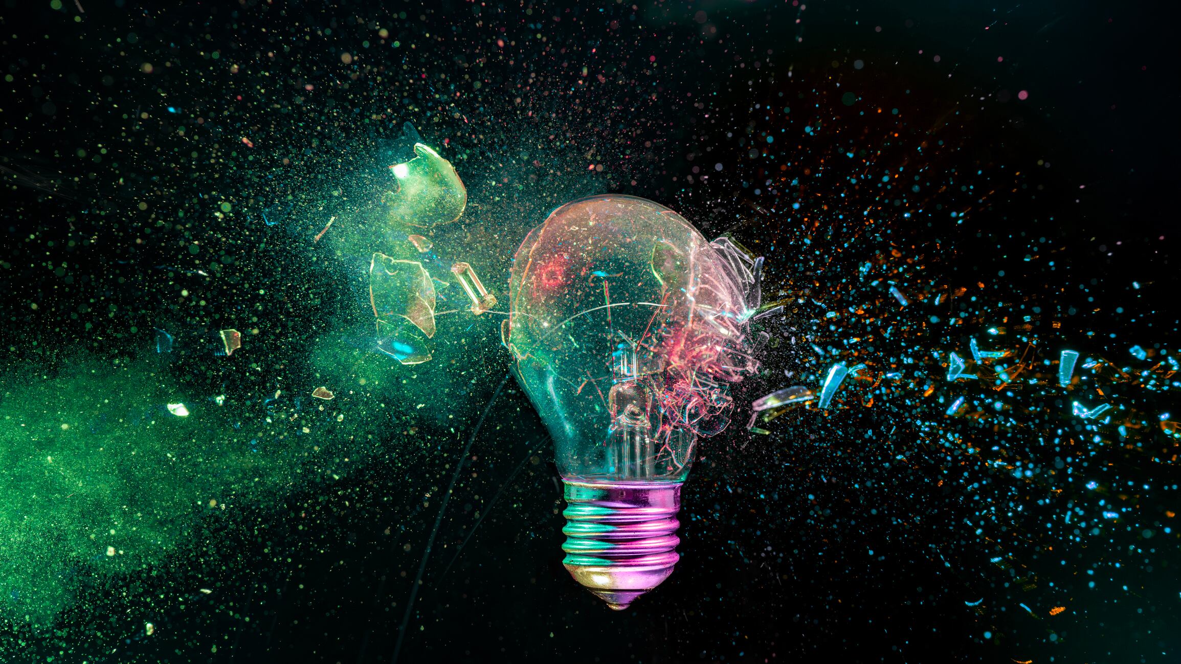 Light bulb explodes into a burst of colorful glass fragments and energetic particles on a black background