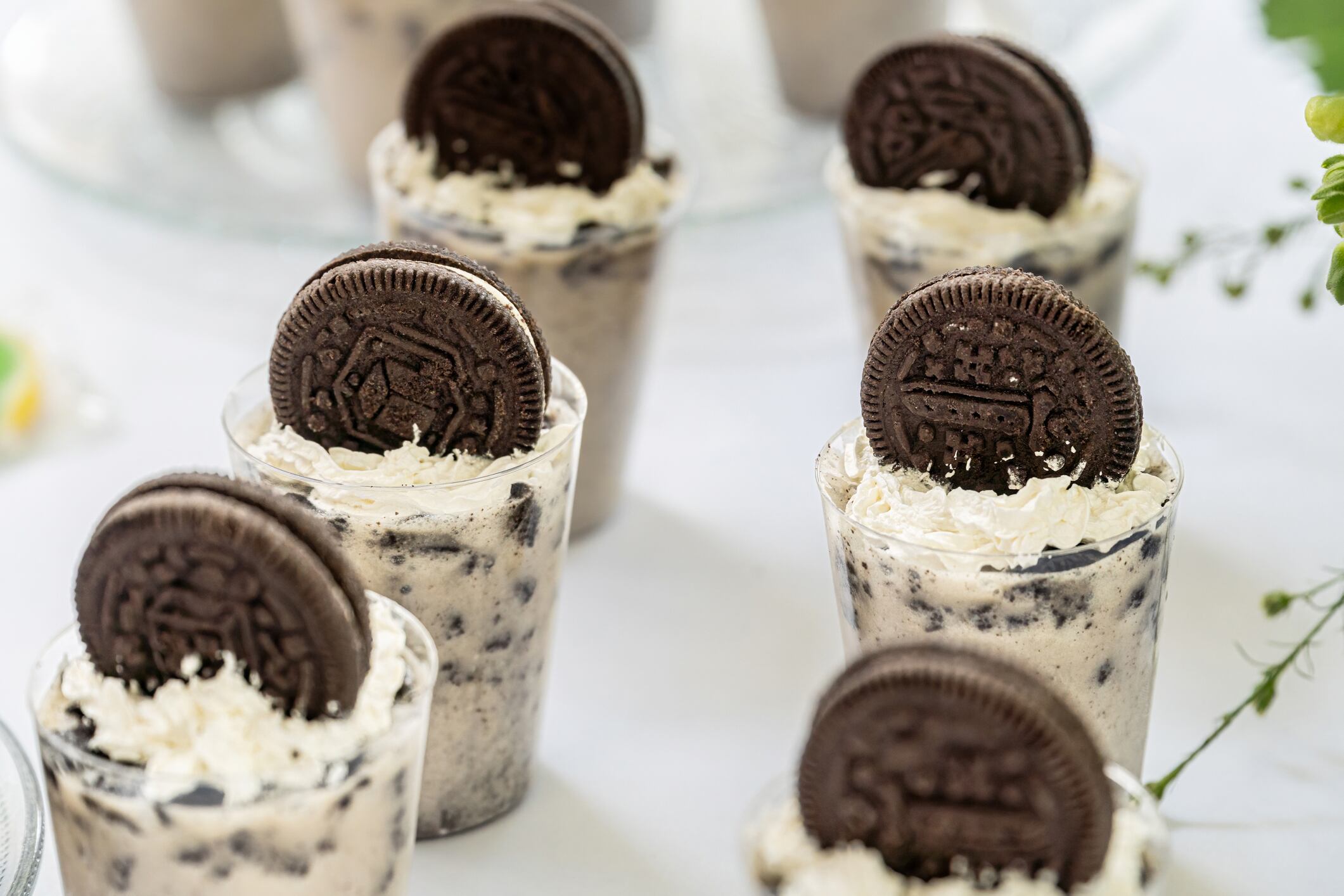 Close-up of individual cookies and cream mousse cups topped with whipped cream and a whole chocolate sandwich cookie. Ideal for catering and dessert buffets.