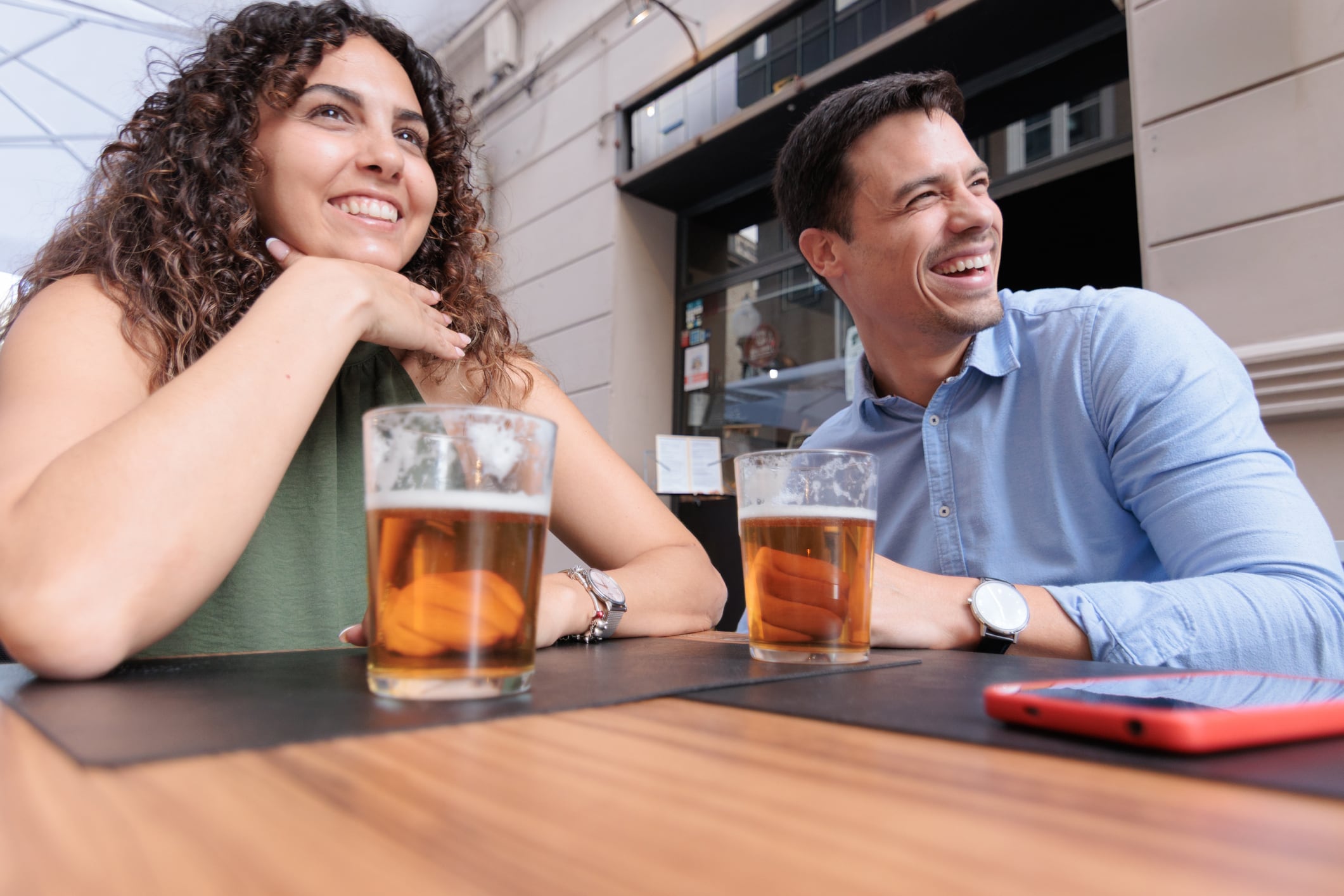 A couple drinking a beer at a bar smiles happily