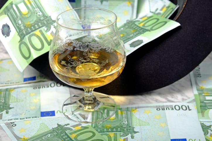 One hundred euro banknotes with a black hat glass of cognac on a marble table on a black background