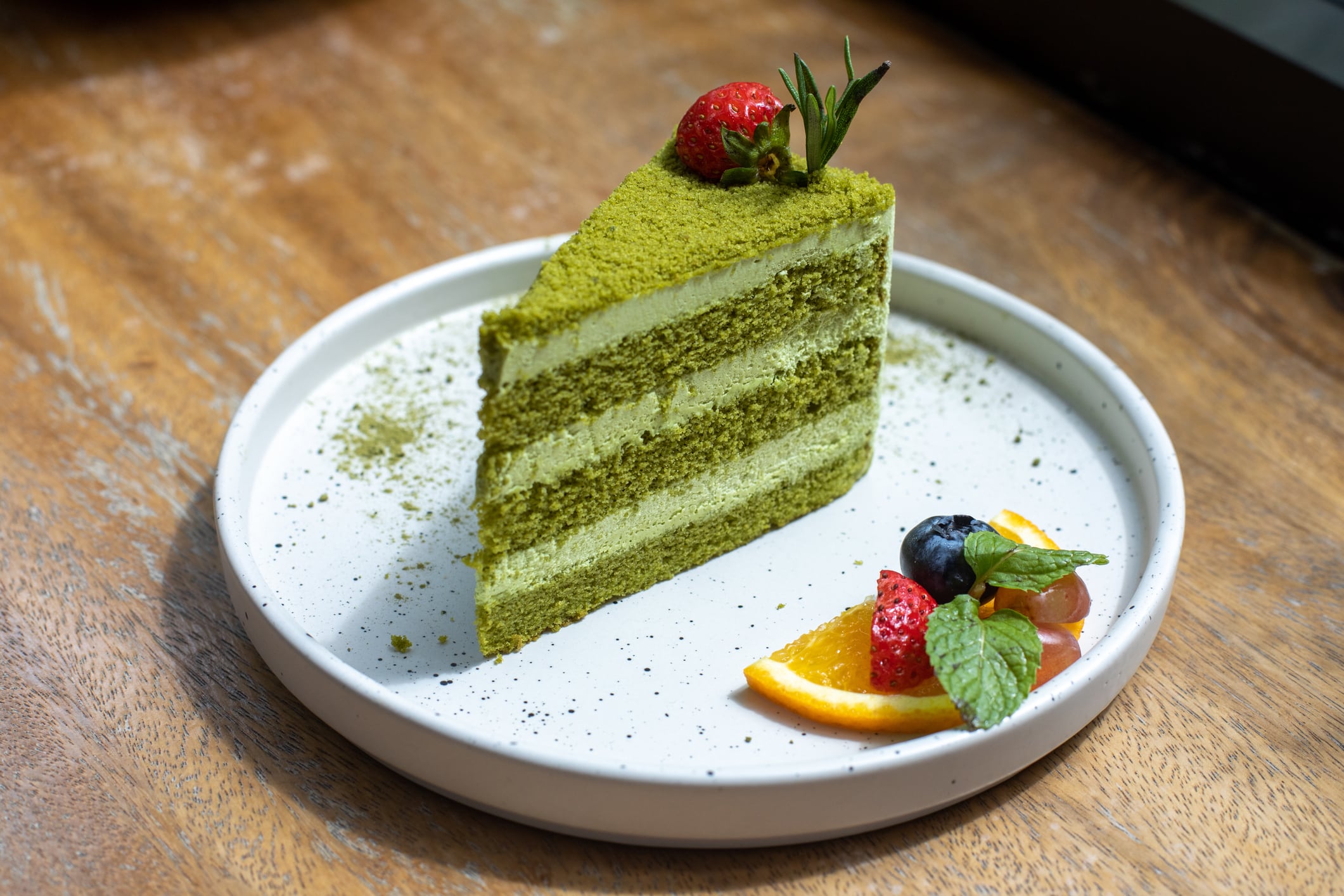 Green cake on a white plate decorated with fruit with wooden background.