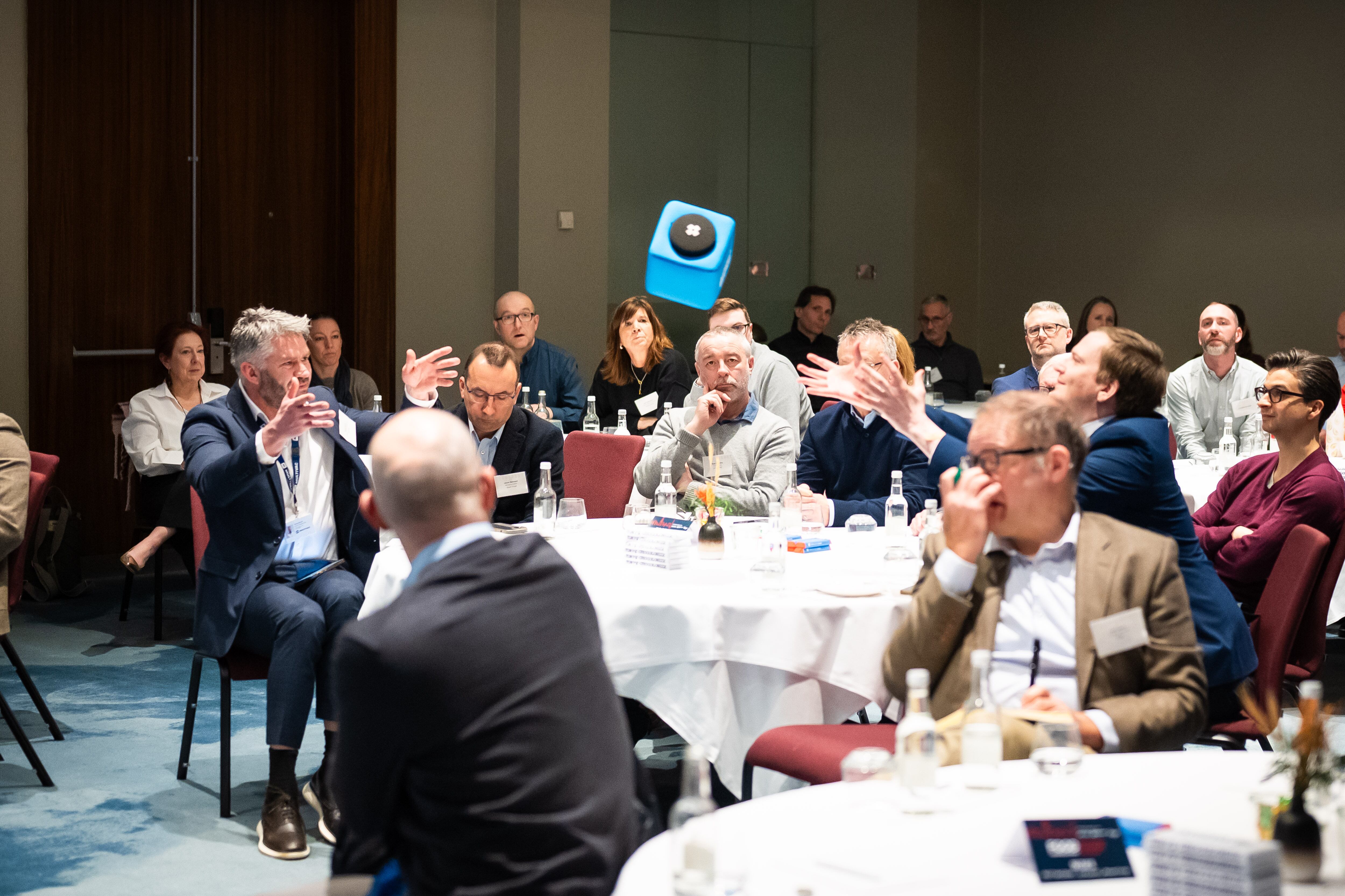 A conference filled with people. A microphone in a soft foam cube being thrown.