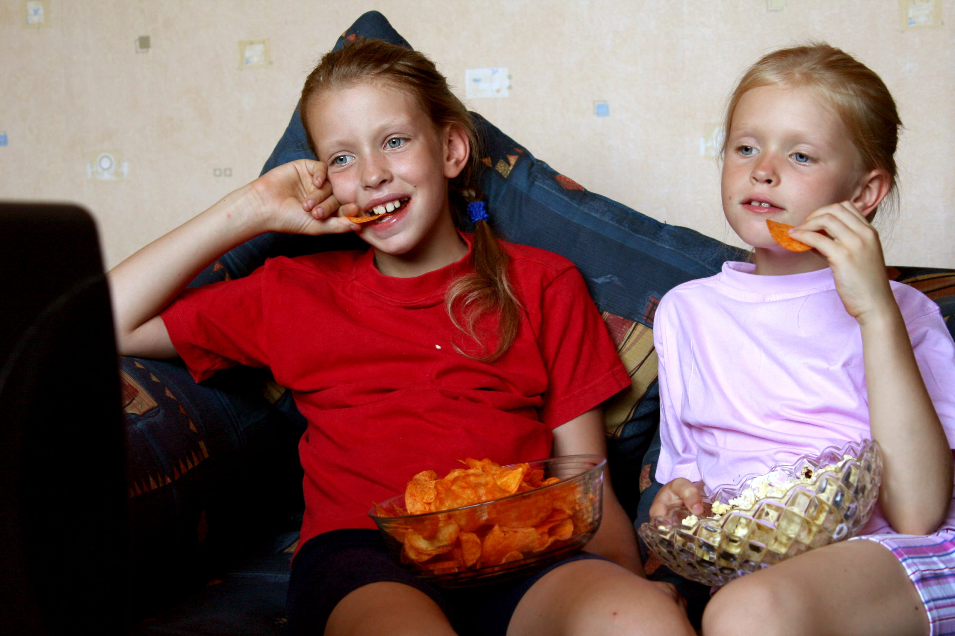 Two children eating snacks in front of the television.
