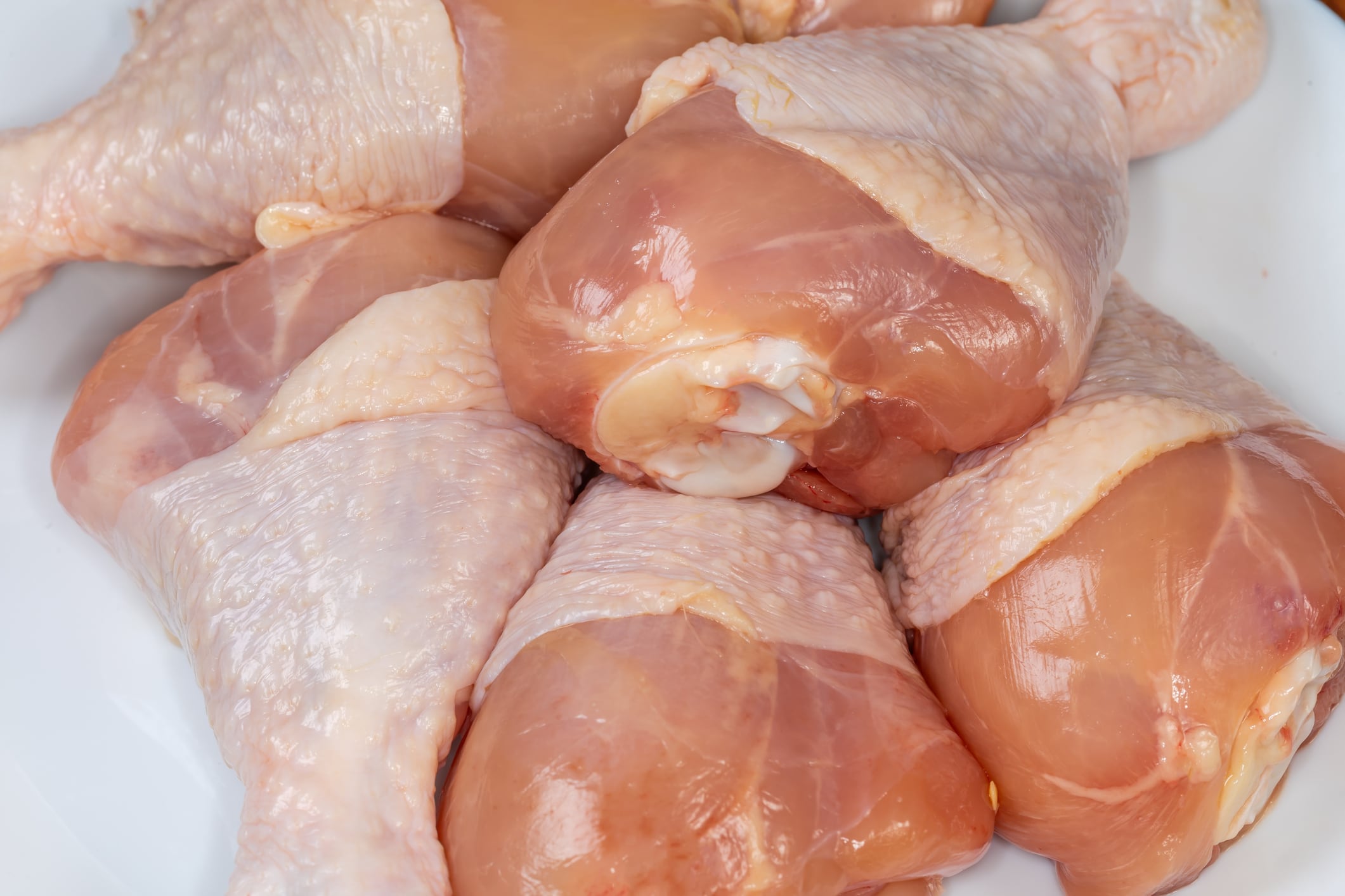 Several raw chicken drumsticks on a white plate, top view of fragment close-up.