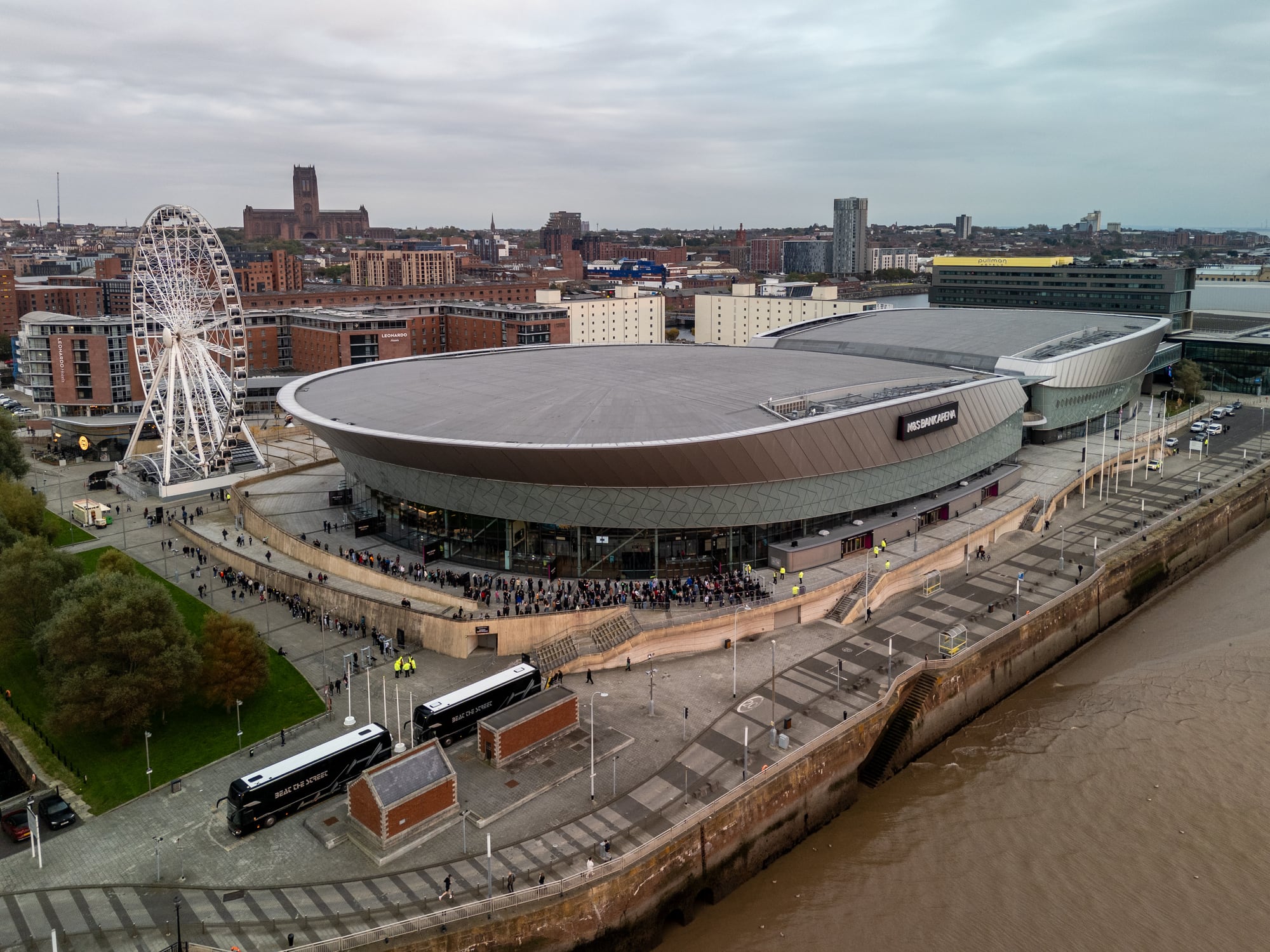 Aerial view of the acc liverpool arena hosting an event with fans queuing outside, on a cloudy day